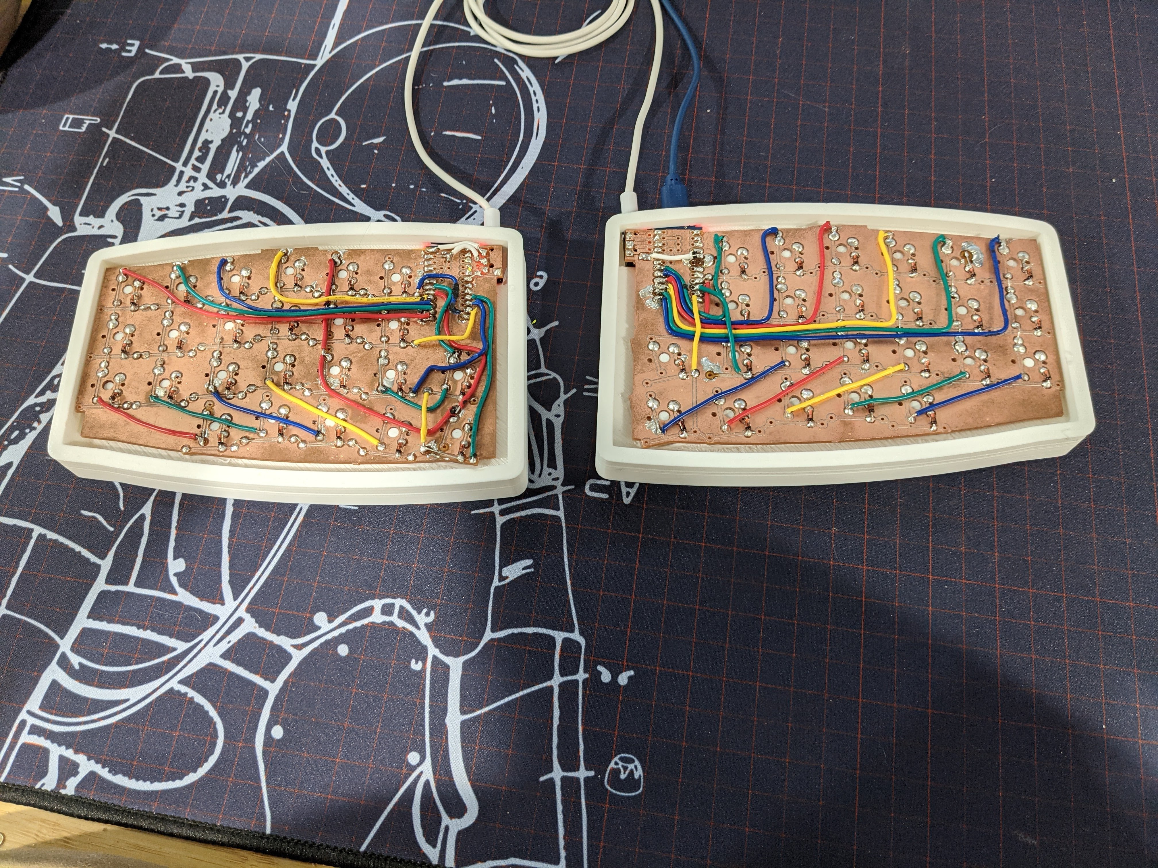 Bottom of keyboard with copper colored plate with white circuit board traces, silver solder bridges and contacts, and colored wires connecting components together. White plastic case around the sides.